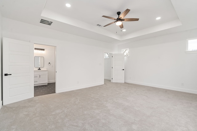 unfurnished bedroom featuring connected bathroom, a raised ceiling, and carpet