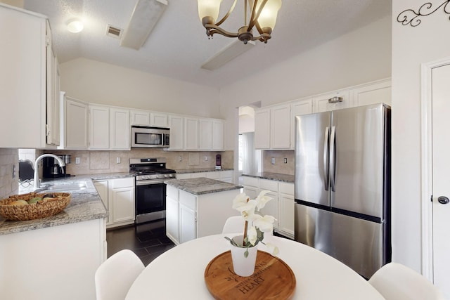 kitchen with appliances with stainless steel finishes, sink, white cabinets, a center island, and light stone counters