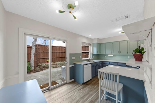 kitchen with sink, tasteful backsplash, light hardwood / wood-style flooring, a textured ceiling, and white dishwasher