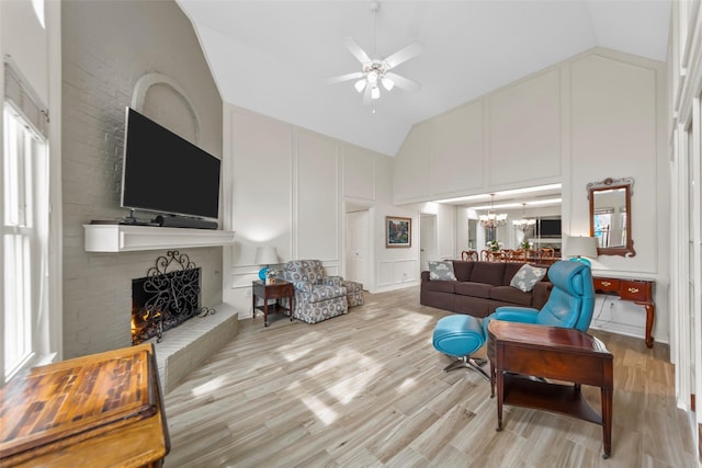 living room with a brick fireplace, ceiling fan with notable chandelier, high vaulted ceiling, and light hardwood / wood-style flooring