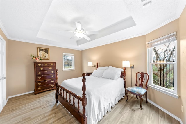 bedroom featuring crown molding, light hardwood / wood-style flooring, ceiling fan, a tray ceiling, and a textured ceiling