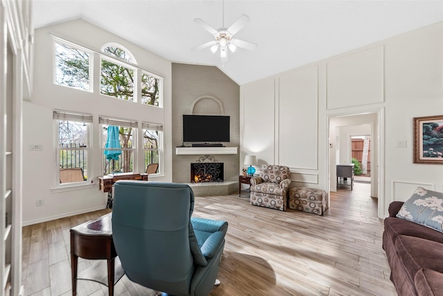 living room featuring ceiling fan, high vaulted ceiling, light hardwood / wood-style floors, and a brick fireplace