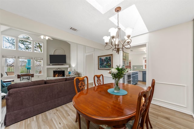 dining space featuring ceiling fan with notable chandelier, a textured ceiling, light hardwood / wood-style floors, and a skylight