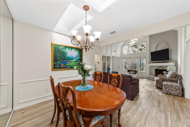 dining area featuring lofted ceiling with skylight, light wood-type flooring, and a chandelier