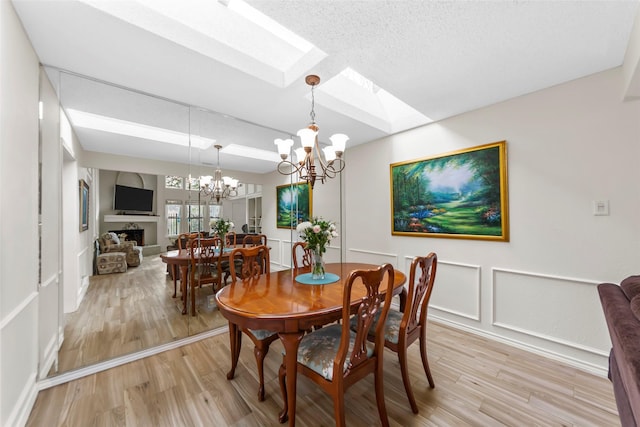 dining area with an inviting chandelier, a skylight, light hardwood / wood-style flooring, and a textured ceiling