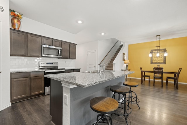 kitchen featuring sink, appliances with stainless steel finishes, a kitchen island with sink, decorative backsplash, and decorative light fixtures