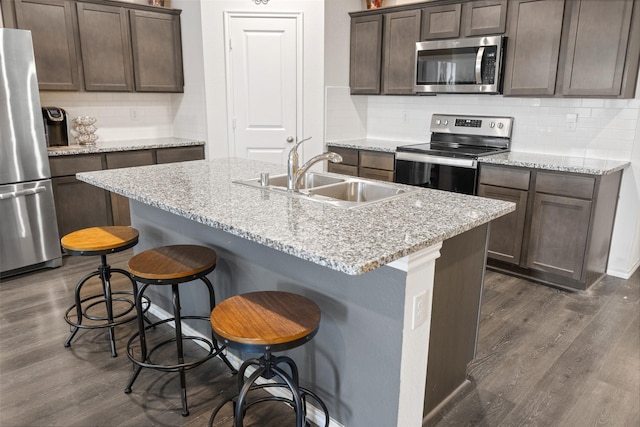 kitchen with appliances with stainless steel finishes, sink, a kitchen bar, a kitchen island with sink, and light stone counters