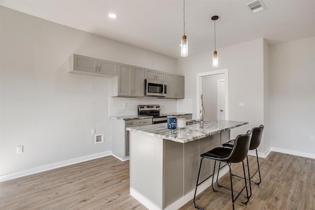 2604 Creekview Dr, Granbury, TX 76048 - kitchen featuring appliances with stainless steel finishes, gray cabinets, light wood finished floors, light stone countertops, and decorative backsplash