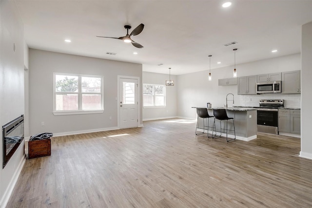 kitchen featuring gray cabinets, an island with sink, appliances with stainless steel finishes, and light hardwood / wood-style floors