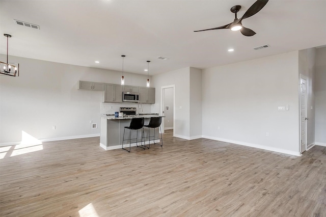 kitchen featuring pendant lighting, gray cabinets, light stone countertops, and appliances with stainless steel finishes