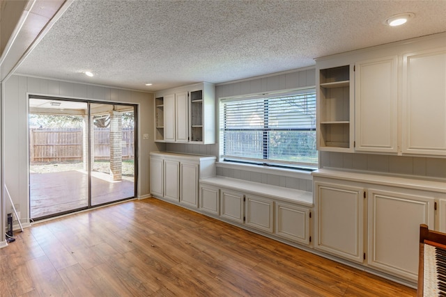 kitchen with ornamental molding, white cabinets, a textured ceiling, and light hardwood / wood-style flooring