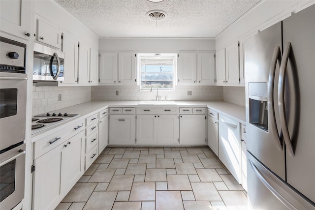 kitchen featuring sink, appliances with stainless steel finishes, backsplash, a textured ceiling, and white cabinets