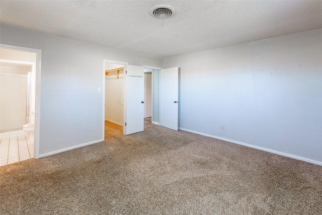 unfurnished bedroom with ensuite bath, carpet flooring, a textured ceiling, a walk in closet, and a closet