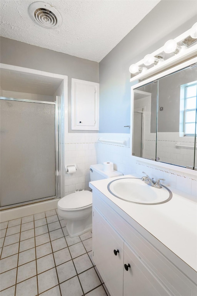 bathroom with tile patterned floors, a shower with door, a textured ceiling, and tile walls