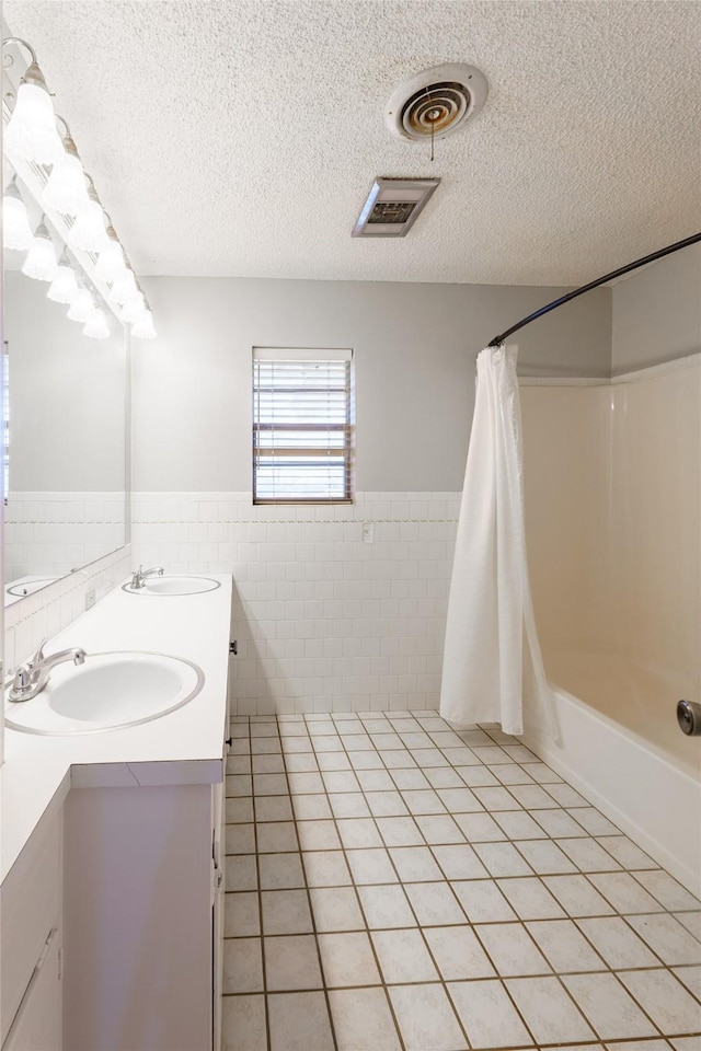 bathroom with tile walls, shower / bath combination with curtain, vanity, tile patterned floors, and a textured ceiling