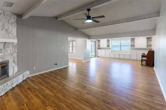 unfurnished living room featuring ceiling fan, hardwood / wood-style floors, vaulted ceiling with beams, a fireplace, and a textured ceiling