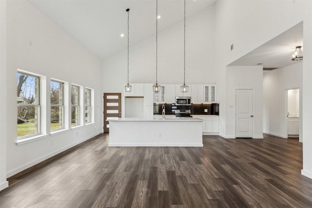 kitchen with dark hardwood / wood-style floors, pendant lighting, white cabinetry, stainless steel appliances, and a center island with sink