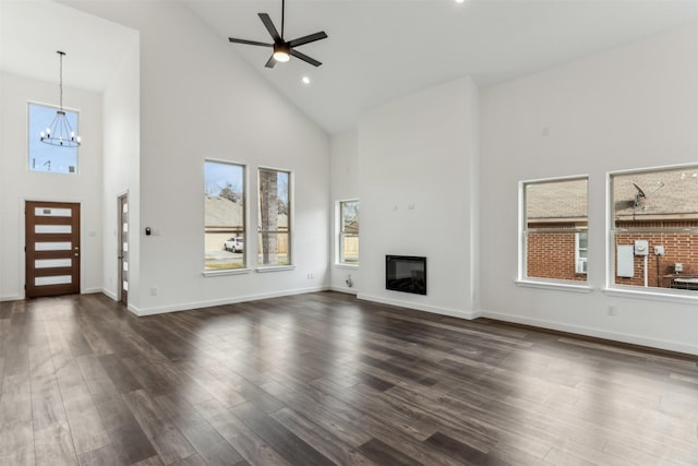 unfurnished living room featuring ceiling fan with notable chandelier, dark wood-type flooring, and high vaulted ceiling