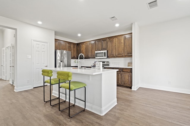 kitchen with sink, a kitchen breakfast bar, a kitchen island with sink, stainless steel appliances, and light hardwood / wood-style floors