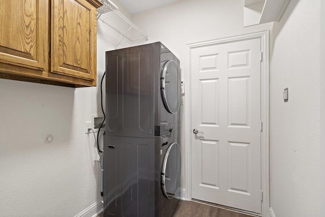 laundry area featuring cabinets, stacked washing maching and dryer, and dark wood-type flooring