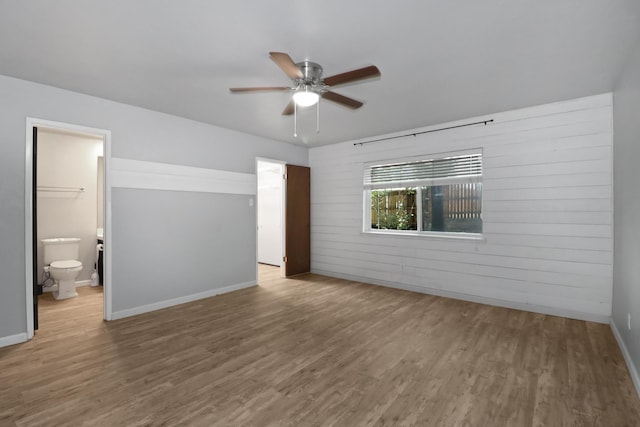 unfurnished bedroom featuring ceiling fan, wooden walls, connected bathroom, and light wood-type flooring