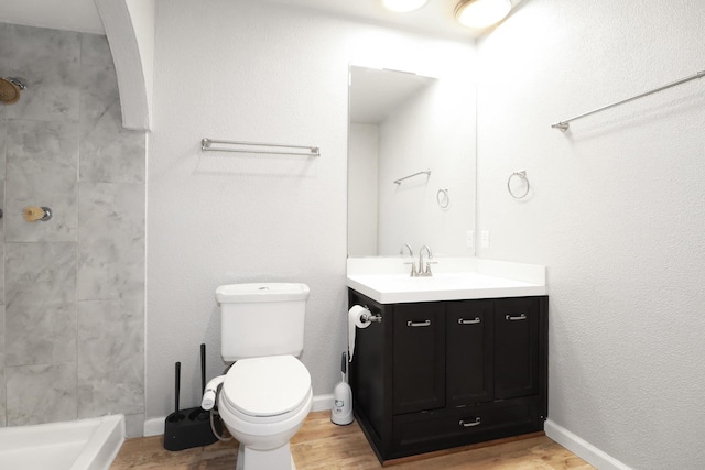 bathroom featuring tiled shower, vanity, toilet, and wood-type flooring