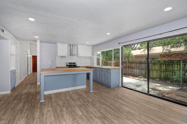 kitchen featuring wood counters, stainless steel range with electric cooktop, white cabinets, wall chimney range hood, and light hardwood / wood-style flooring