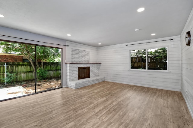 unfurnished living room featuring a fireplace, light hardwood / wood-style floors, wooden walls, and plenty of natural light