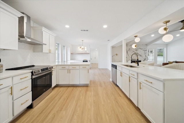 kitchen with decorative light fixtures, white cabinetry, sink, stainless steel appliances, and wall chimney exhaust hood