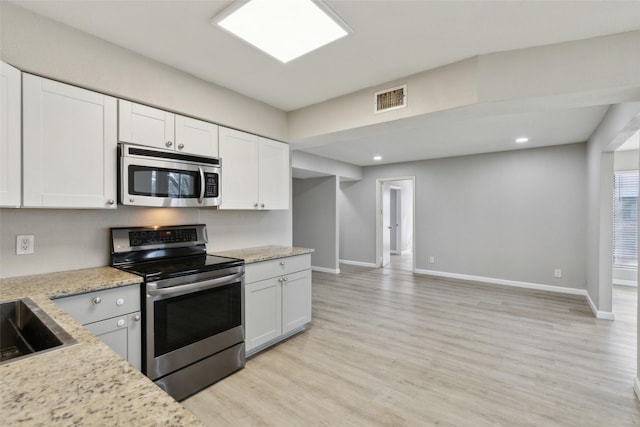 kitchen with light stone countertops, stainless steel appliances, white cabinets, and light wood-type flooring