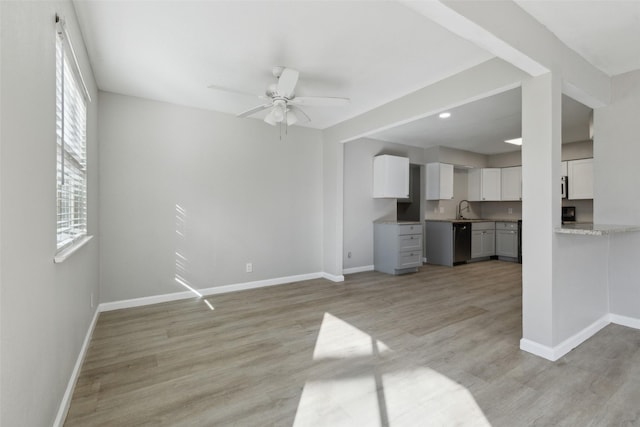 unfurnished living room featuring ceiling fan, sink, and light wood-type flooring