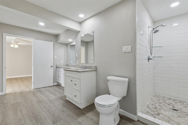 bathroom featuring toilet, a tile shower, vanity, hardwood / wood-style flooring, and ceiling fan