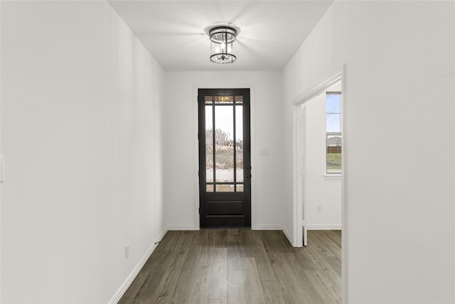 doorway to outside featuring a notable chandelier, baseboards, and wood finished floors