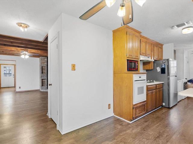 kitchen with dark hardwood / wood-style floors, stainless steel fridge, oven, ceiling fan, and a brick fireplace