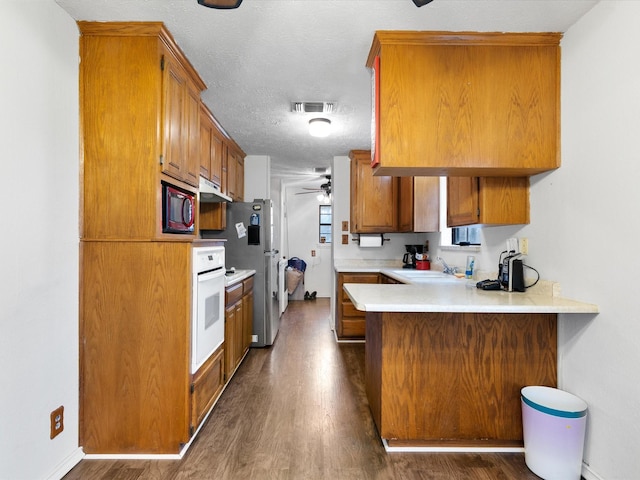 kitchen with dark wood-type flooring, sink, stainless steel refrigerator, kitchen peninsula, and white oven