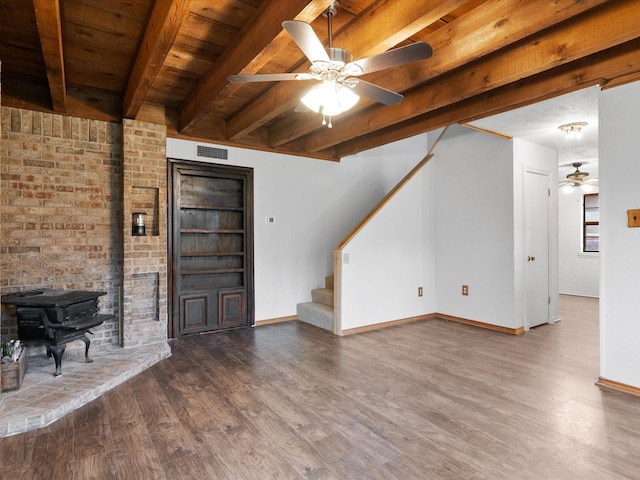 unfurnished living room featuring ceiling fan, beam ceiling, hardwood / wood-style floors, and a wood stove