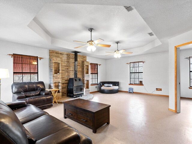 living room with ceiling fan, a raised ceiling, a textured ceiling, and a wood stove
