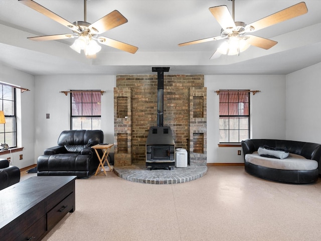 living room featuring a raised ceiling, ceiling fan, and a wood stove