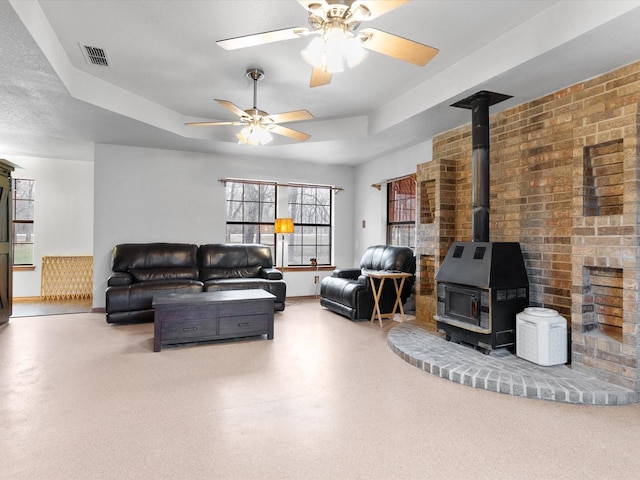 living room featuring a raised ceiling, a wood stove, and ceiling fan