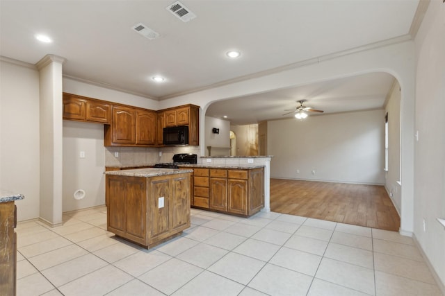 kitchen featuring a kitchen island, light tile patterned floors, ceiling fan, black appliances, and crown molding