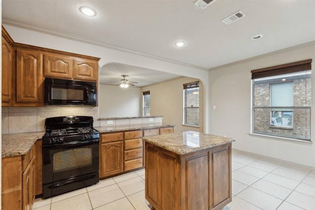 kitchen featuring backsplash, light stone counters, ornamental molding, black appliances, and a kitchen island