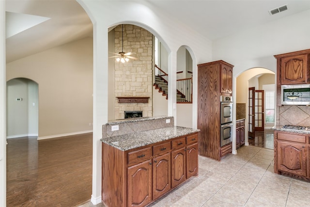 kitchen featuring lofted ceiling, ceiling fan, stainless steel appliances, light stone countertops, and decorative backsplash