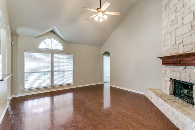 unfurnished living room featuring a stone fireplace, dark wood-type flooring, high vaulted ceiling, and ceiling fan