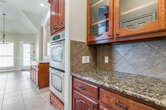 kitchen featuring pendant lighting, tasteful backsplash, light tile patterned floors, light stone countertops, and stainless steel double oven