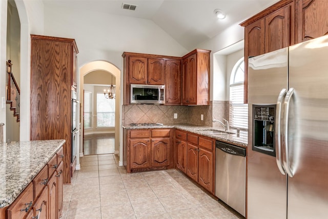 kitchen with vaulted ceiling, sink, decorative backsplash, stainless steel appliances, and light stone countertops