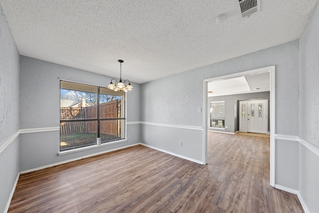 unfurnished dining area featuring hardwood / wood-style flooring, a chandelier, and a textured ceiling