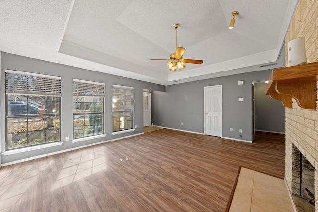 unfurnished living room featuring hardwood / wood-style flooring, a tray ceiling, a brick fireplace, and a textured ceiling