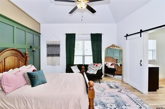 bedroom featuring ceiling fan, a barn door, lofted ceiling, and light wood-type flooring