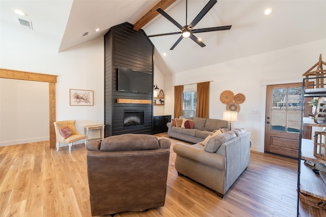 living room with a healthy amount of sunlight, a large fireplace, beam ceiling, and light hardwood / wood-style floors