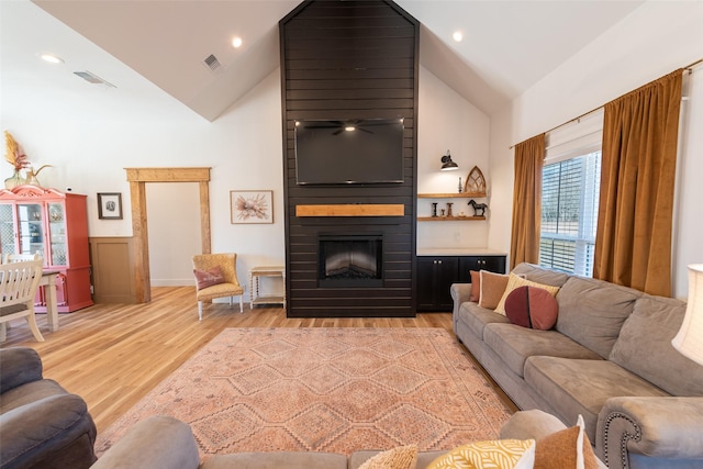 living room featuring light hardwood / wood-style flooring, high vaulted ceiling, and a large fireplace